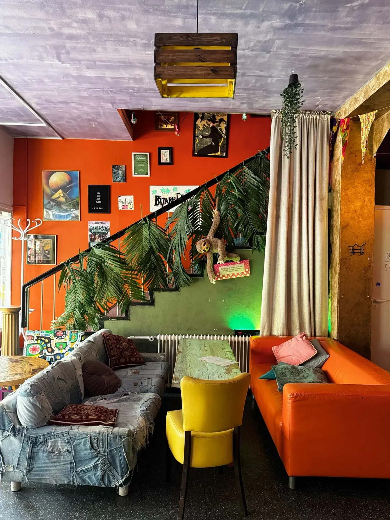 Värikäs oleskelutila, jossa on oranssi seinä, portaiden kaide koristeltu tekopalmunlehdillä, oranssi sohva, keltainen tuoli ja farkkukankaalla päällystetty nojatuoli.